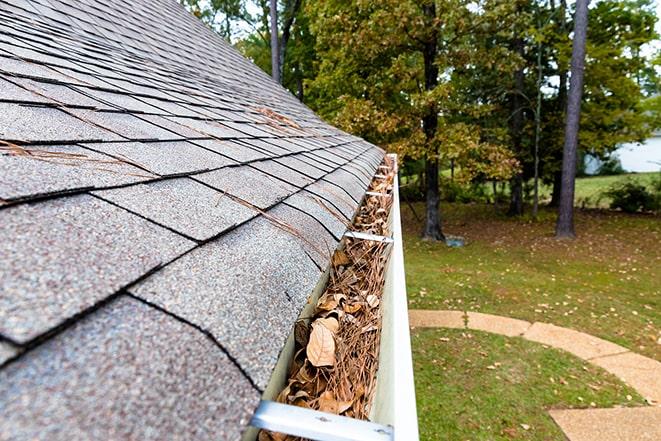 a hand scooping out dirt and twigs from a clogged gutter